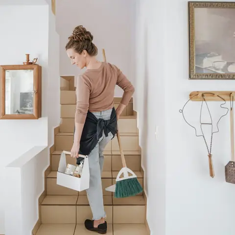 Femme montant un escalier avec un panier de produits et un balai