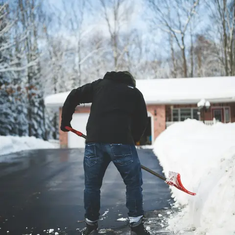 Personne déneigeant à la pelle l’entrée d’une maison en hiver